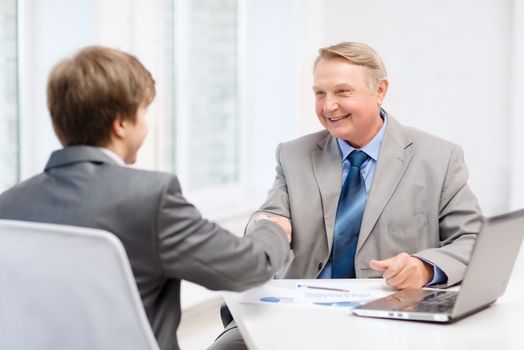 business, technology and office concept - older man and young man shaking hands in office