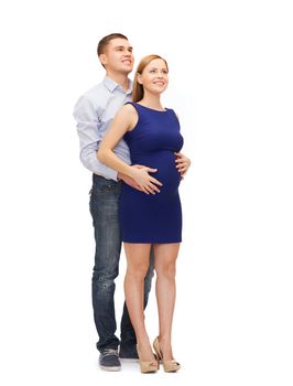 pregnancy, parenthood and happiness concept - happy young family expecting child looking up