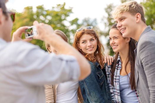 summer holidays, electronics and teenage concept - group of smiling teenagers taking photo with digital camera outside