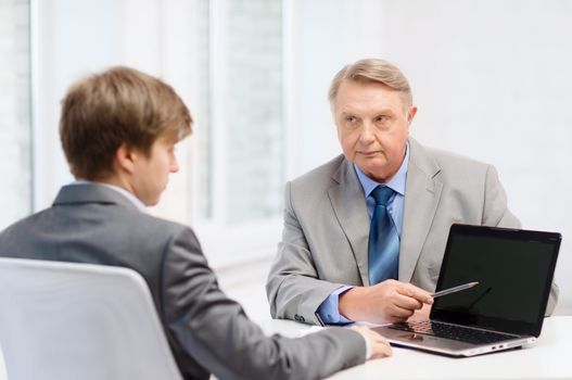 business, advertisement, technology and office concept - older man and young man with laptop computer in office