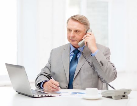 business, technologym communication and office concept - busy older businessman with laptop, charts, coffee and telephone in office