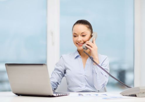 business, technology and communication concept - smiling businesswoman with phone, laptop and files in office