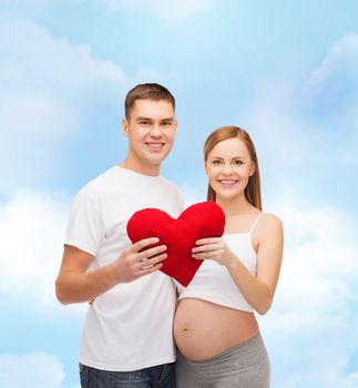 pregnancy, parenthood, love and happiness concept - happy young family expecting child with big red heart