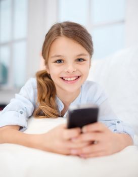 home, leisure, technology and internet concept - little student girl with smartphone at home