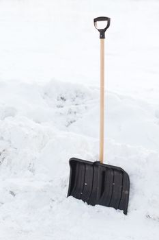 winter and equipment concept - black snowshowel with wooden handle in snow pile