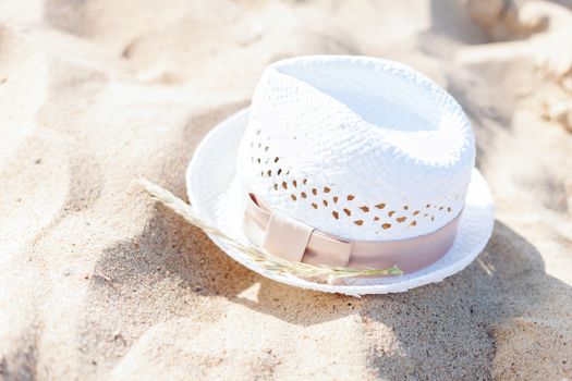 hats and summer concept - white straw hat lying in the sand on the beach