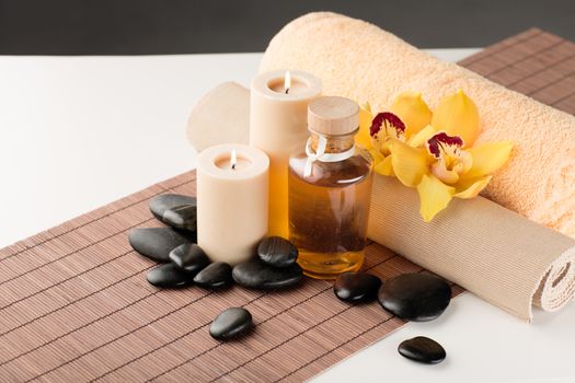 spa, health and beauty concept - closeup of essential oil, massage stones, candles and orchid flower