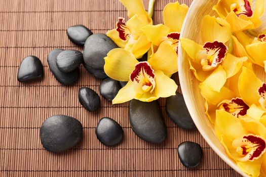 spa, heath and beauty concept - massage stones with orchid flowers on mat