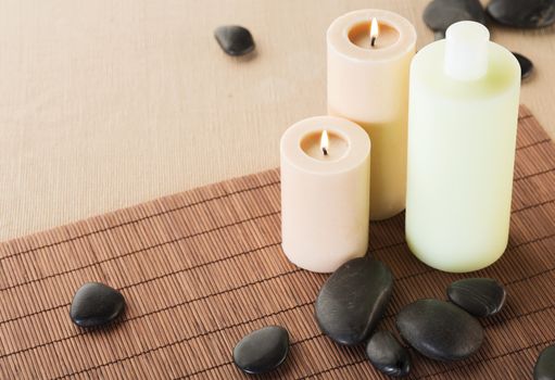 spa, health and beauty concept - closeup of shampoo bottle, massage stones and candles