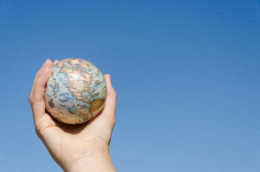 stylized global earth model toy in hand on blue sky background, north America continent