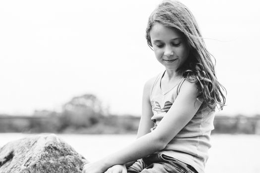 Girl daydreaming sitting on a rock by a river in black and white