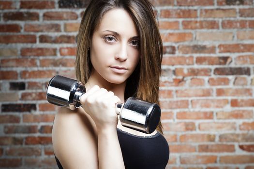 Portrait of Young fit woman lifting dumbbells and looking at camera