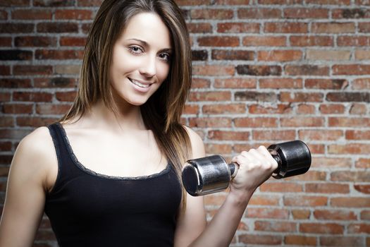 Portrait of Young smiling sexy woman lifting dumbbells on brick background