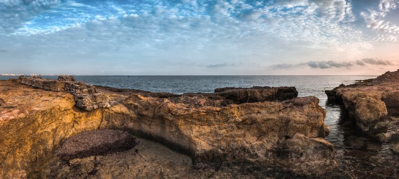 Sunset over the Sea and Rocky Coast with Ancient Ruins