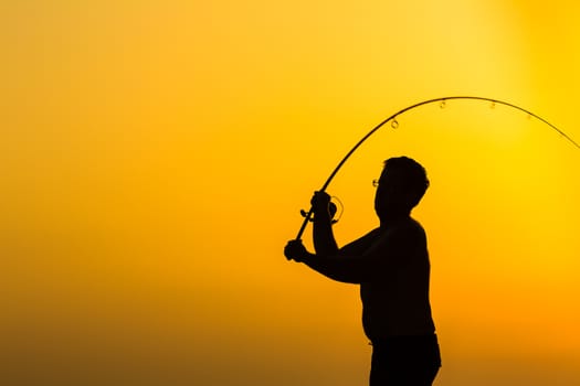 Fisherman silhouette on the beach at colorful sunset