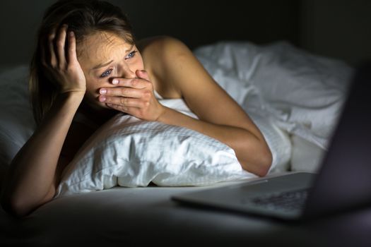 Pretty young woman watching something awful/sad on her laptop in bed