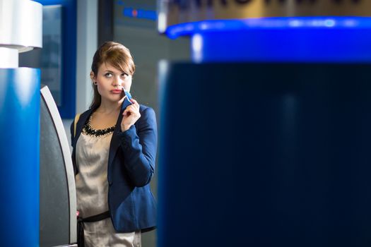 Pretty, young woman withdrawing money from her credit card in at an ATM (shallow DOF; color toned image)