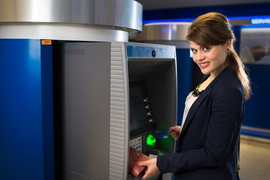 Pretty, young woman withdrawing money from her credit card in at an ATM (shallow DOF; color toned image)