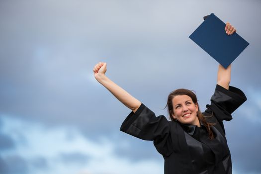 Pretty, young woman celebrating joyfully her graduation - spreading wide her arms, holding her diploma, savouring her success (color toned image; shallow DOF)