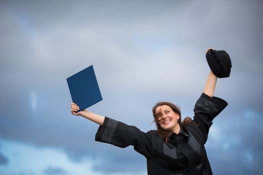 Pretty, young woman celebrating joyfully her graduation - spreading wide her arms, holding her diploma, savouring her success (color toned image; shallow DOF)