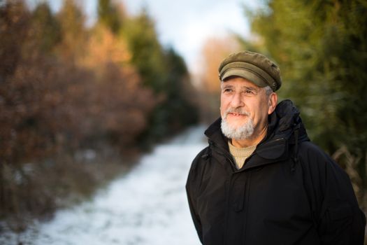 Portrait of a senior man, outdoor on a snowy forest path. Enjoying the crisp fresh air, watching the Sun go down.