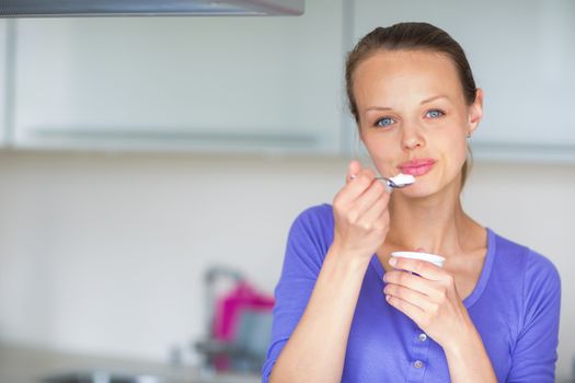 Happy young woman eating yogurt in kitchen