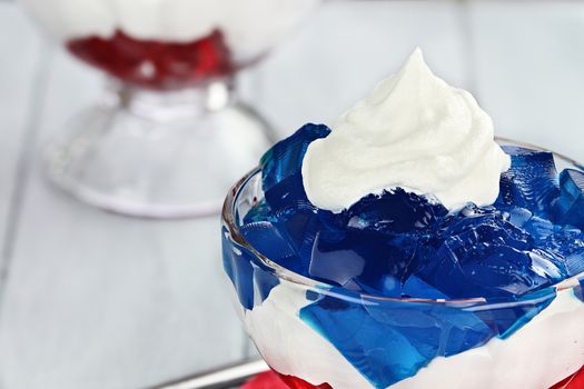 Gelatin layered dessert of cubes of red and blue jello with white fluffy whipped cream for the Fourth of July holiday. Shallow depth of field.