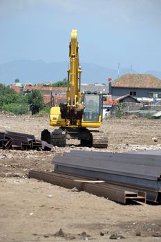 yellow backhoe in front of steel bar stack