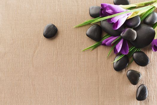 spa, heath and beauty concept - massage stones with flowers on mat