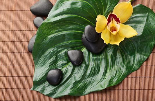 spa, heath and beauty concept - massage stones with orchid flowers on mat