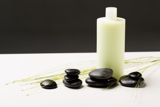 spa, health and beauty concept - closeup of shampoo bottle, massage stones and green plant