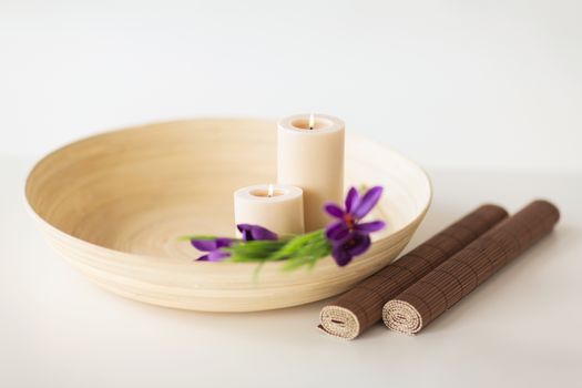 spa, health and beauty concept - candles and iris flowers in wooden bowl and bamboo mat