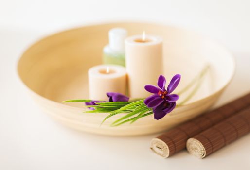 spa, health and beauty concept - candles and iris flowers in wooden bowl and bamboo mat