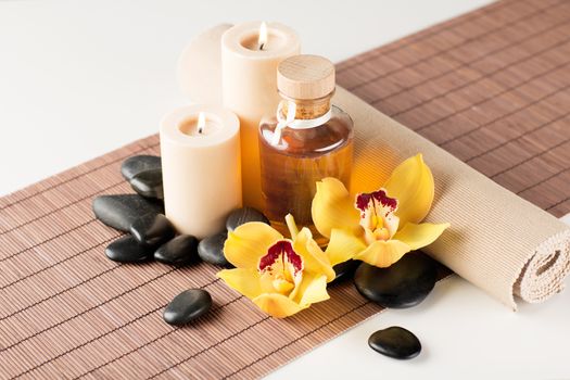 spa, health and beauty concept - closeup of essential oil, massage stones, candles and orchid flower