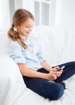 home, leisure, technology and internet concept - little student girl with smartphone at home