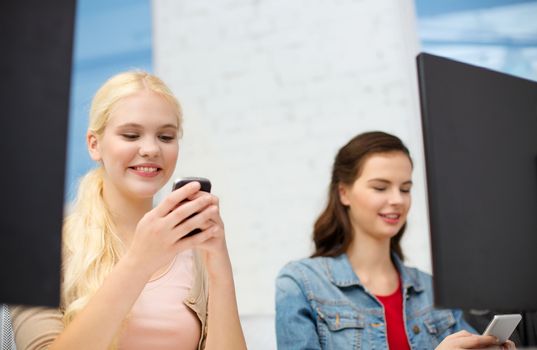 school, education, technology and internet concept - two teens with smartphones in computer class at school