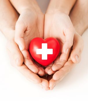 family health, charity and medicine concept - male and female hands holding red heart with cross sign