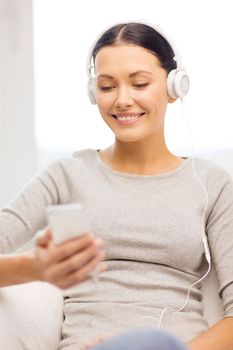 home, technology, communication and internet concept - woman sitting on the couch with smartphone and headphones at home