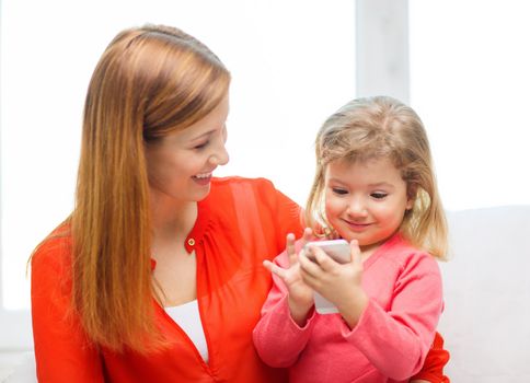 family, children, parenthood, technology and internet concept - happy mother and daughter with smartphone at home