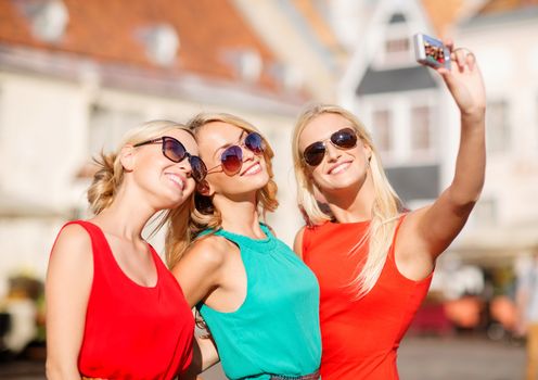 holidays, tourism and modern technology concept - three beautiful girls taking picture with digital camera in the city