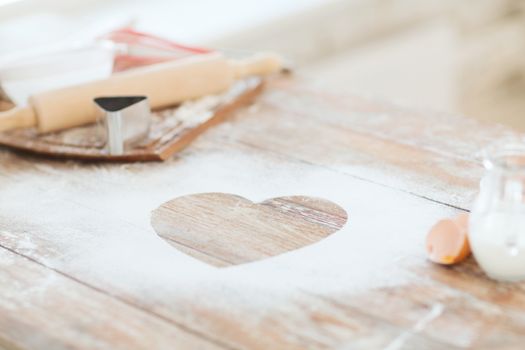 cooking and love concept - close up of heart of flour on wooden table at home