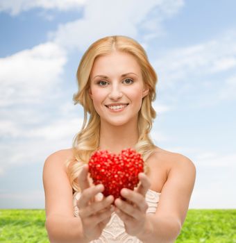 health, charity and love concept - smiling woman giving small red heart