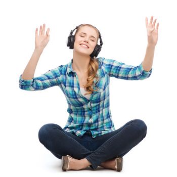 music and technology concept - smiling young woman sitting on floor and listeting to music with headphones