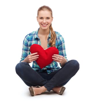 happiness and people concept - smiling young woman in casual clothes sitiing on floor and holding red heart