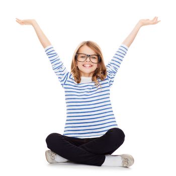 happiness and people concept - smiling girl in eyeglasses sitting on floor and waving hands
