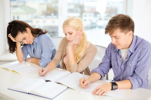 school and education concept - group of tired students with notebooks at school