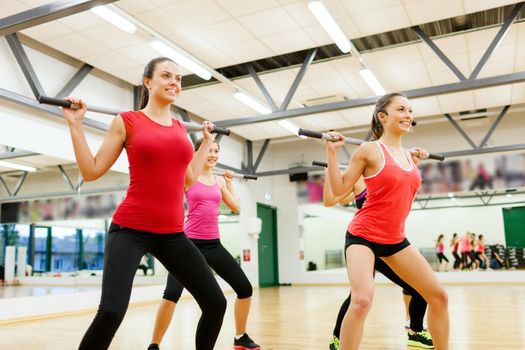 fitness, sport, training, gym and lifestyle concept - smiling trainer in front of the group of people working out with barbells in the gym