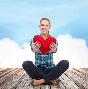 happiness and people concept - smiling young woman in casual clothes sitiing on floor and holding red heart