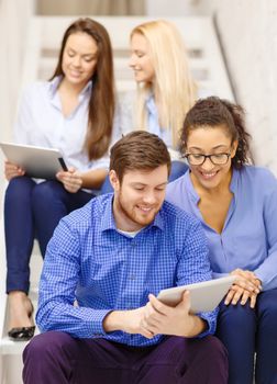 business, technology and startup concept - smiling creative team with tablet pc computer sitting on staircase