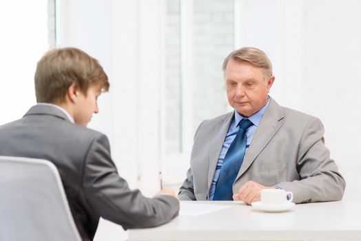 business, technology and office concept - older man and young man signing papers in office